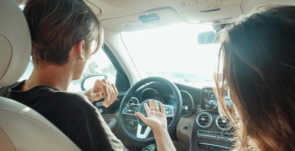 Twee personen zitten in auto terwijl bestuurder met handen gebaart tijdens het rijden