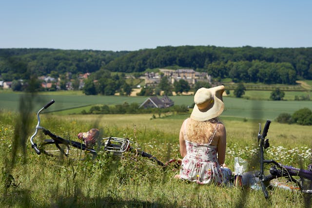 Een vrouw die met haar fiets in het gras zit en over het Limburgs landschap kijkt